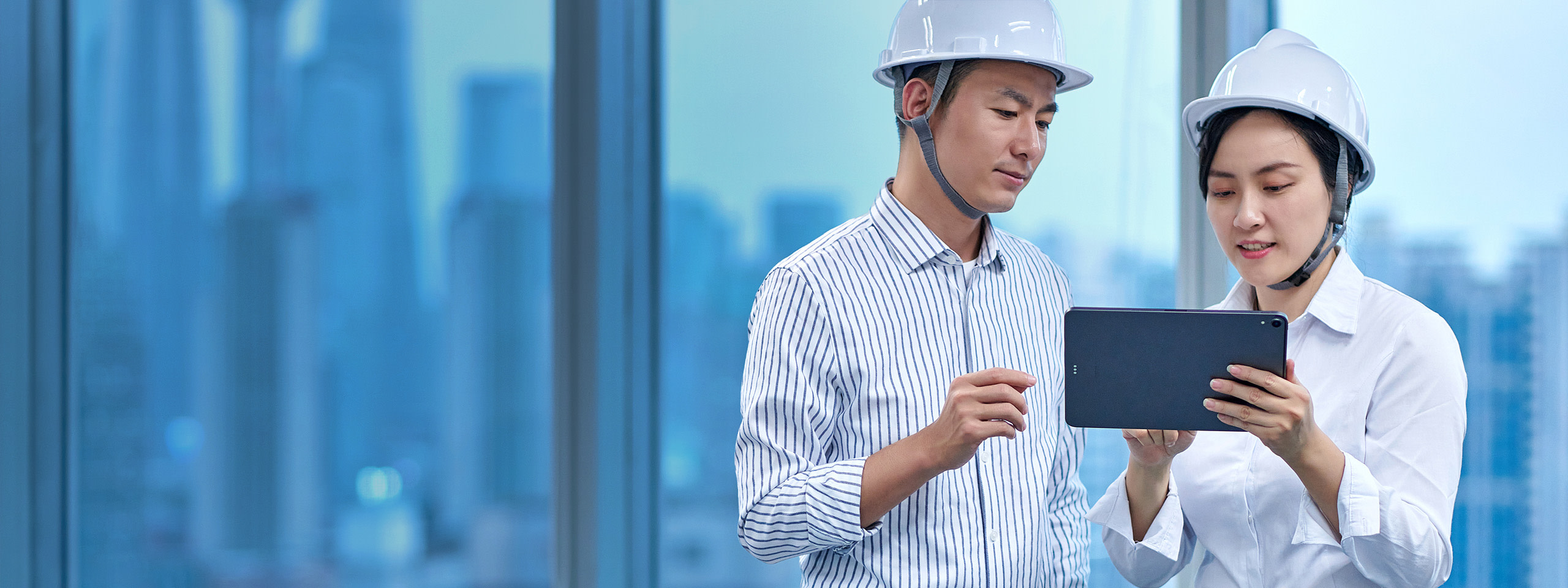 A man and a woman wearing safety helmets and using a tablet